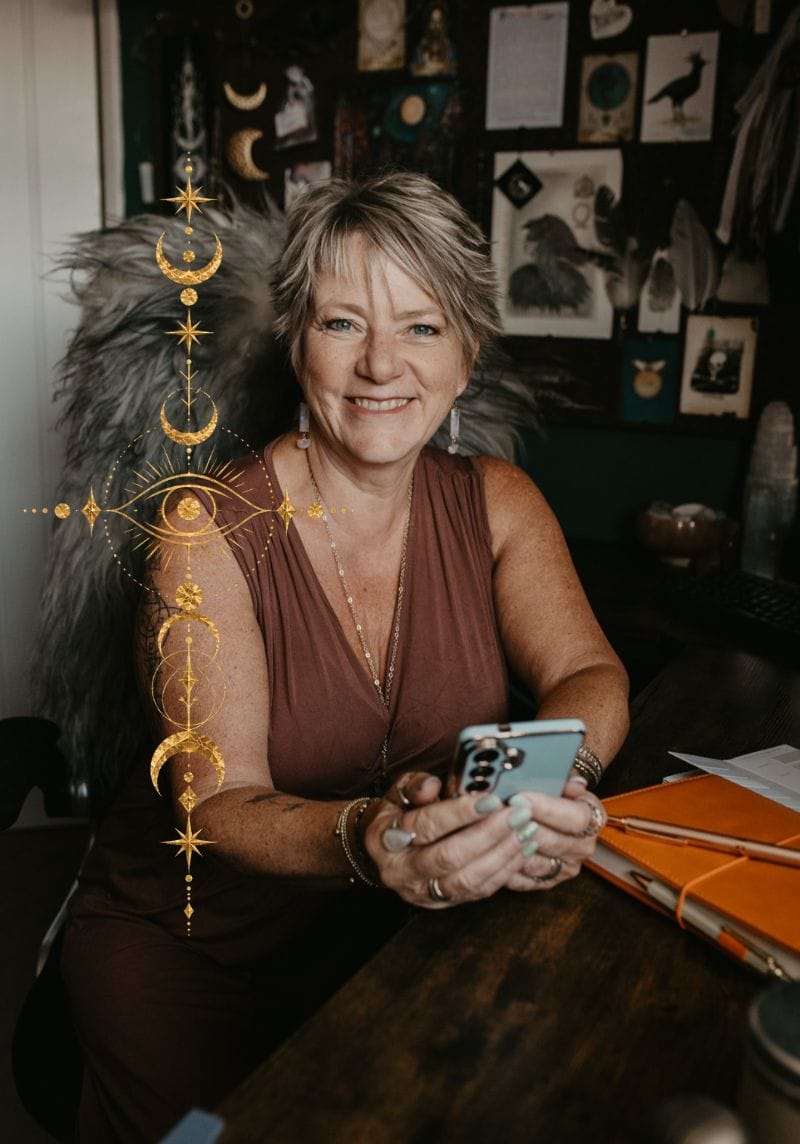 Tania Meacher smiling at her desk, holding her phone in her creative workspace.