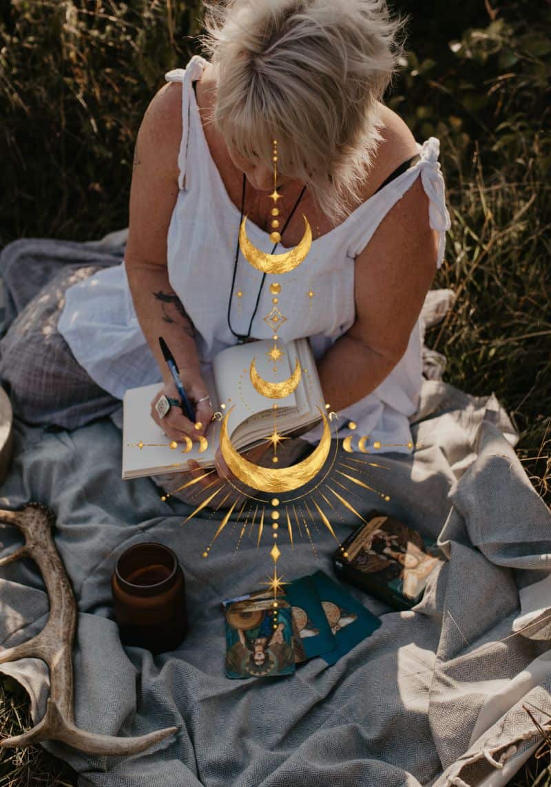Tania Meacher writing in a notebook while seated outdoors on a blanket, with oracle cards and a gold moon design in the foreground.