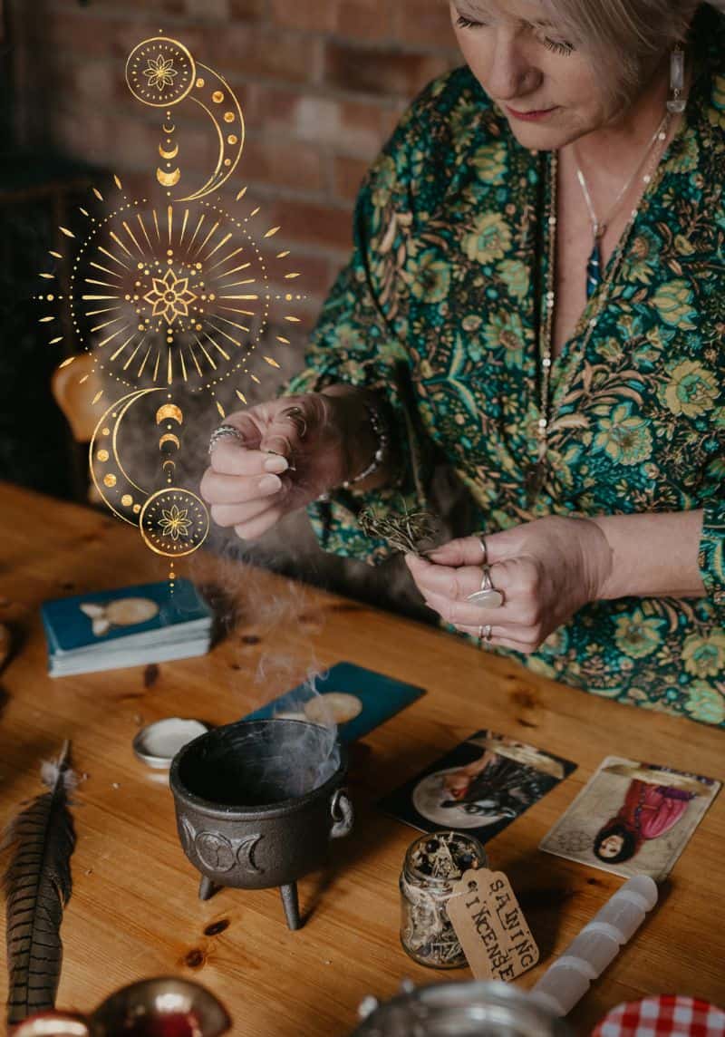 Holistic wellbeing website design - Tania meacher (1) Tania Meacher holding a smoking bundle of herbs above a wooden table with a cauldron and oracle cards.