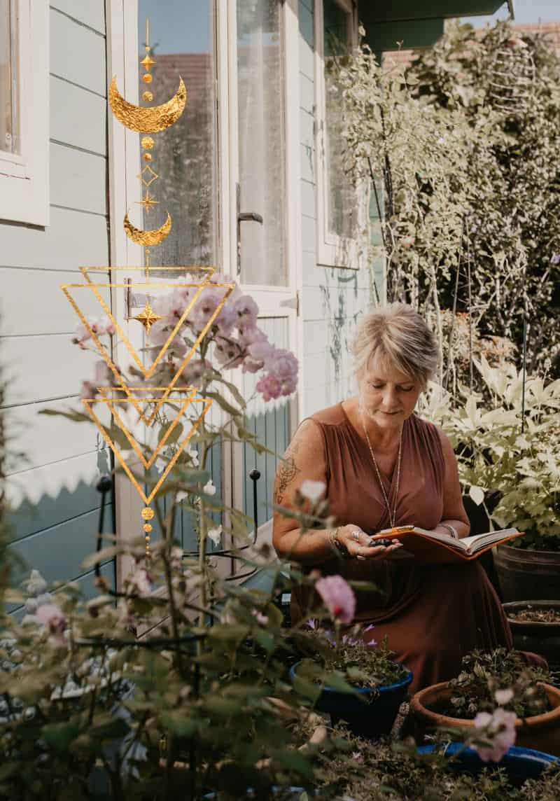 Tania Meacher sitting outside among flowers and plants, writing in an open notebook.