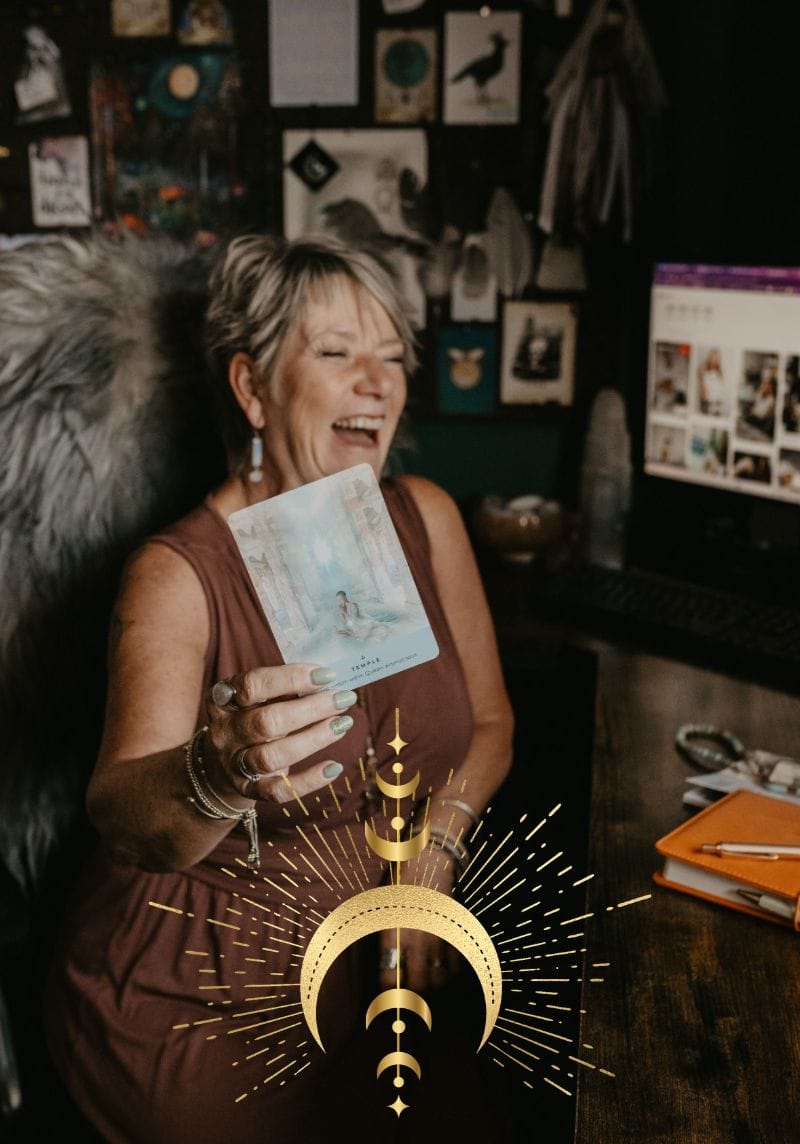 Tania Meacher - Creative Witch Designs (1) Tania Meacher laughing while holding a booklet in her creative workspace, with a gold crescent moon design overlaid on the photograph.