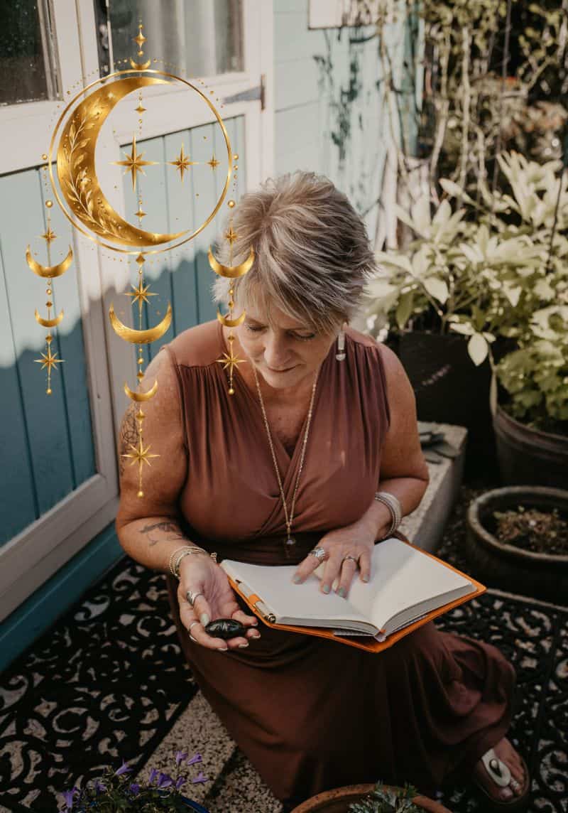 Tania Meacher sitting outside her garden studio, looking down at an open notebook on her lap.