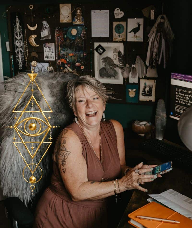 Tania Meacher - WordPress Websites for Reiki Healers (1) Tania Meacher laughing at her desk while holding her phone, with an orange notebook beside her.