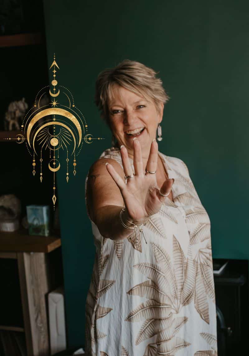 Tania Meacher standing with one hand raised against a dark green wall, with a gold crescent moon design beside her.