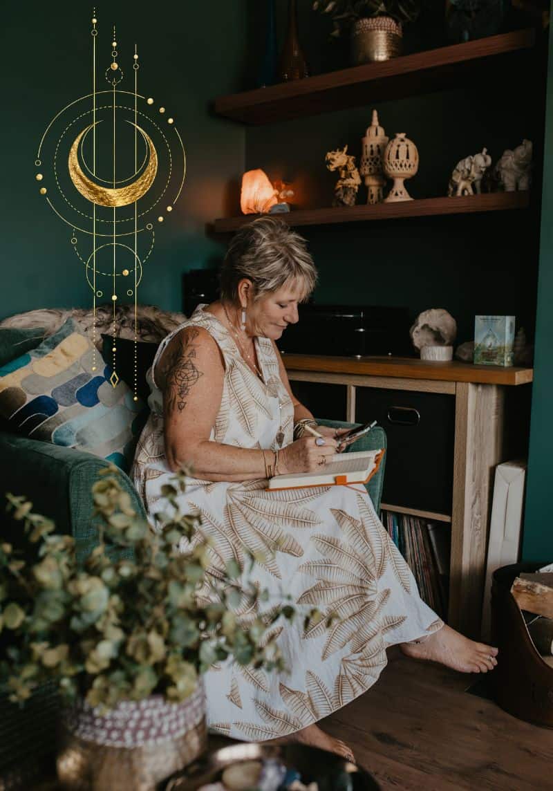 Tania Meacher sitting in an armchair, looking at her phone with an open notebook on her lap.